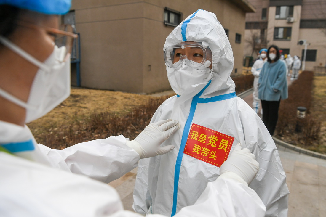 在長春市參與疫情防控的工作人員幫助同伴在防護服上粘貼“我是黨員我帶頭”的標識（4月4日攝）。